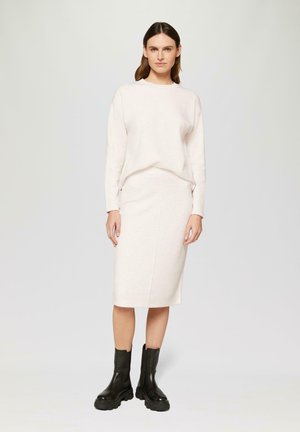 Pull léger beige et jupe midi en tissu doux, associés à des bottines noires chunky. Texture lisse avec des détails de design minimalistes.
