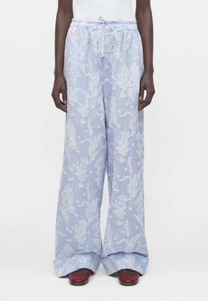 Jasnoniebieskie spodnie z szerokimi nogawkami z białym kwiatowym haftem, elastycznym pasem ze sznurkiem, noszone z ciemnoczerwonymi płaskimi butami.