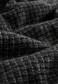 Zwart en grijs textiel met een geruit patroon, voorzien van zachte, fuzzy vezels die een warme en uitnodigende uitstraling creëren.