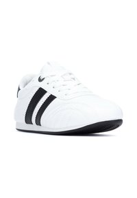 Zapatillas deportivas blancas con rayas negras, hechas de material sintético. Presentan una puntera redondeada, paneles laterales texturizados y un cierre con cordones.