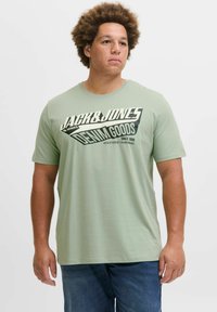 Tricou din bumbac verde, cu un imprimeu �îndrăzneț în nuanțe de negru și crem, ce citește „JACK & JONES DENIM GOODS” pe față. Decupaj rotund la gât, mâneci scurte.