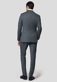 Szary garnitur w prążki o dopasowanym kroju, z jednym rozcięciem i kontrastującymi czarnymi butami. Teksturowana tkanina podkreśla detale wizualne.