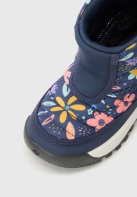 Nærbilde av en blå støvel med et fargerikt blomsterdesign, som fremhever livlige blomster i rosa, gul og grønn mot en mørk bakgrunn.