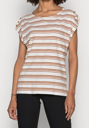 Femme portant un haut blanc à manches courtes avec des rayures horizontales marron et des détails de boutons sur les épaules, assorti à un pantalon noir.