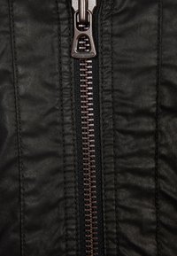 Svart läderjacka med en framträdande metallisk dragkedja, med en texturerad yta och subtil glans, detaljerad med inslag av vävt tyg.