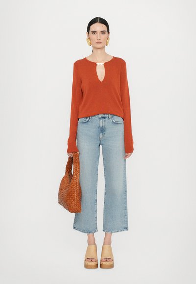 Rust knit sweater with a keyhole neckline, light blue wide-leg jeans, tan platform sandals, and a woven brown handbag.