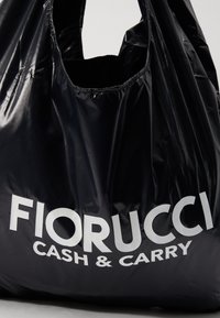 Schwarze Plastiktüte mit glänzender Oberfläche. Mit großen weißen Schriftzügen "FIORUCCI CASH & CARRY." Enthält zwei Griffe.