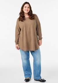 Brūns garo piedurknu džemperis ar sānu pogām, apvienots ar gaiši zilajiem platajiem džinsiem un melnajām kurpēm. Mīksts audums ar brīvu piegriezumu.