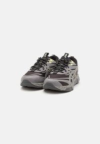 Black and gray athletic shoes with mesh and synthetic overlays, featuring a thick sole, textured accents, and reflective details on the laces.