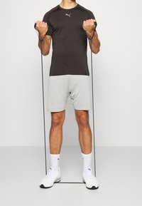 Svart tränings t-shirt med grå accenter, matchad med ljusgrå texturerade shorts. Personen håller i träningsband och har på sig vita sneakers.