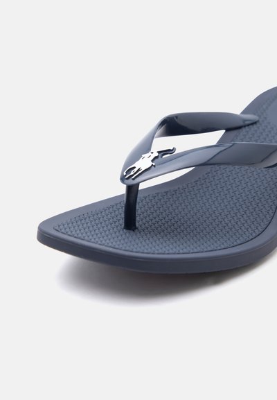 Σκούρο μπλε σανδάλι σαγιονάρες με υφασμένο πέλμα και γυαλιστερές λουρίδες σε σχήμα V, με ένα μικρό ασημένιο έμβλημα λογότυπου στο λουρί.