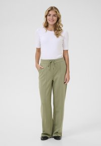 Pantalons légers de couleur olive avec une taille à cordon de serrage, au design large et dotés de deux poches latérales. Associés à un haut blanc ajusté.