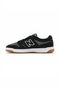 Zapatillas de deporte de ante negro y malla con acentos blancos, que cuentan con una suela de goma y un prominente logo 'N' en el lado. Diseño de perfil bajo.
