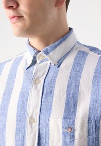 Lichtblauw en wit gestreept overhemd met korte mouwen, met een button-down kraag, een borstzak en geborduurd logo detail. Zachte, gestructureerde stof.