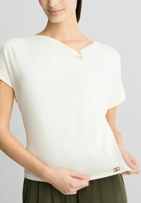 Kratki rukavi, off-white gornji dio napravljen od mekog materijala, s V-izrezom s metalnim naglaskom i dekorativnom kopčom na donjem rubu.