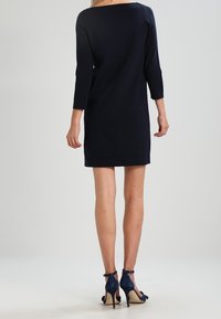 Mörkblå stickad klänning med trekvartslånga ärmar och rak skärning, med en bred halsringning och en mjuk textur. Höga klackar i blått mocka.