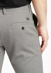 Pantaloni grigi realizzati in tessuto strutturato, con una tasca posteriore con bottone e una piccola etichetta del marchio sulla vita.