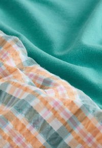 Tissu en tilleul doux à côté d'un tissu à carreaux pastel froissé avec un motif à carreaux orange, rose, bleu et blanc.