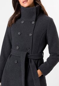 Abrigo de mezcla de lana gris oscuro con un alto cuello, diseño de doble botonadura y un cinturón atado en la cintura. Botones negros acentúan el frente.