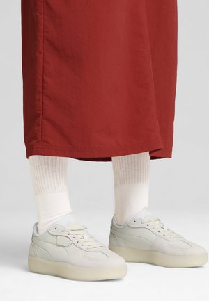 Baskets blanches avec une texture lisse, un bout arrondi et une semelle épaisse translucide, associées à des chaussettes légères à côtes et à une jupe rouge.