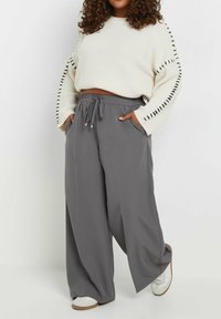 Breda grå byxor med elastiskt midjeband och sidofickor; kombinerat med en krämfärgad tröja med ribbad textur och svarta accenter.