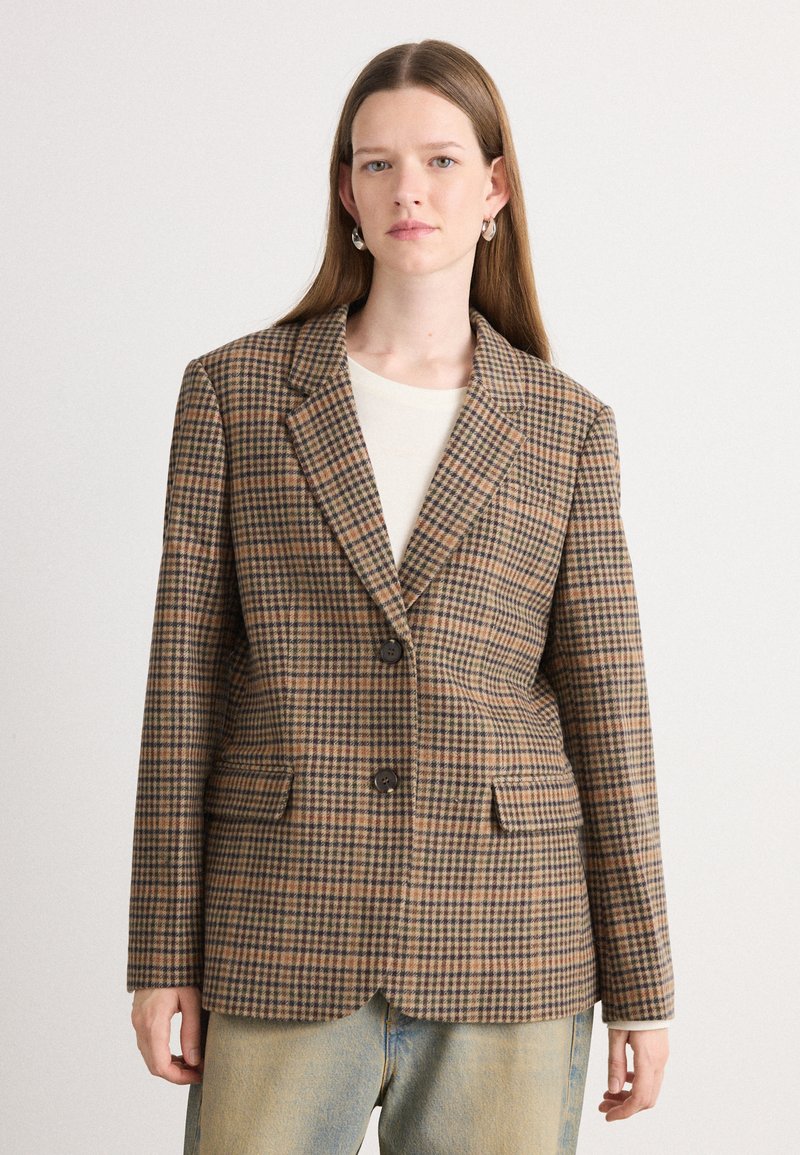 Blazer à carreaux marron avec revers cranté, deux poches avant et deux boutons ; associé à un haut crème et un jean bleu clair.