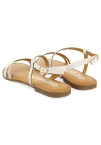 Chanclas planas con correas sintéticas blancas, una plantilla de cuero marrón claro y una suela de goma marrón clara con un detalle de cierre de hebilla.