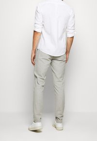 Vit långärmad skjorta och ljusgrå byxor i linne, med slim fit och utan synliga mönster, kombinerat med vita sneakers.