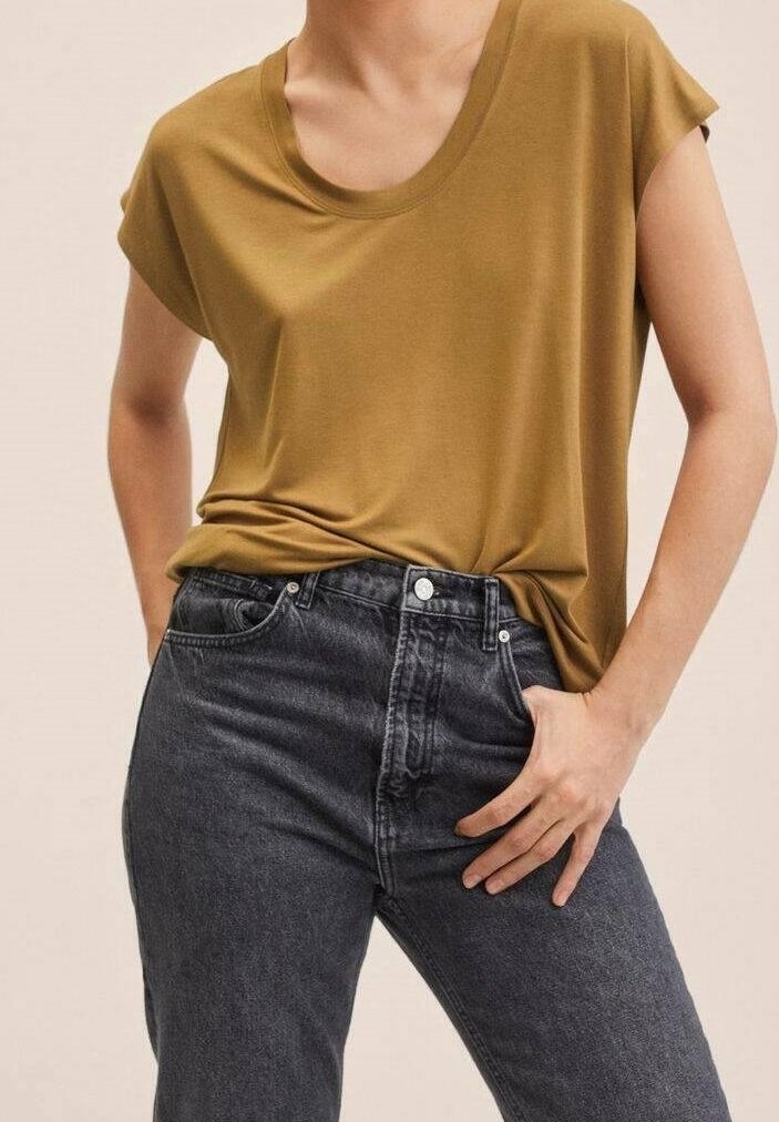 T-shirt jaune moutarde à manches courtes avec un col dégagé, associé à un jean gris foncé taille haute, présentant un tissu texturé.