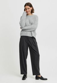 Pull en laine grise, floconneux, avec des manches longues et une coupe décontractée, associé à un pantalon noir plissé et des mocassins noirs. Design simple et contemporain.