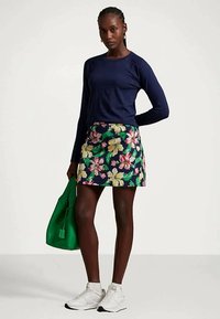 Ναυτικό μακρυμάνικο μπλουζάκι, μίνι φούστα με λουλούδια σε πράσινο, ροζ και κίτρινο χρώμα σε σκούρο φόντο, συνδυασμένη με πράσινη τσάντα και λευκά αθλητικά παπούτσια.