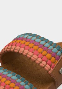 Κοντινό πλάνο λουριού σανδαλιού με υφαντό ύφασμα σε μπλε, μοβ, πορτοκαλί, ροζ και ροδακινί χρώματα πάνω σε πάτο από φελλό.