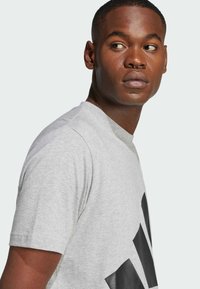 Γκρι βαμβακερό t-shirt με κοντά μανίκια, ραμμένο κολάρο σε στυλ crew, και μεγάλο μαύρο γραφικό σχέδιο. Λείος υφή με άνετη εφαρμογή.