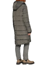 Manteau matelassé long et gris avec un design matelassé horizontal, capuche attachée, poignets élastiques et ourlet arrondi, associé à un jean gris et des bottes beiges.