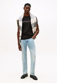 Grå og hvit stripete genser henger over en svart Tommy Hilfiger t-skjorte. Lyseblå jeans med rette ben. Sorte loafers. Nøytral bakgrunn.