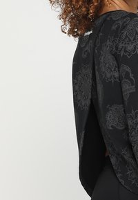 Maglietta nera a maniche lunghe con un motivo discreto, scollatura rotonda e design con schiena spaccata. Realizzata in tessuto morbido e leggero.