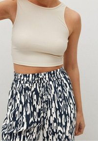 Crop top côtelé beige avec un col montant, associé à un pantalon ample bleu marine et blanc à motifs, doté d'une taille élastique.