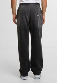 Pantalones de chándal gris oscuro hechos de una tela suave, con un bolsillo trasero y cinturilla elástica, con una silueta relajada y de pernera ancha.