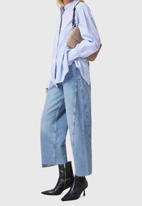 Chemise boutonnée rayée bleu clair, culottes en denim délavé à coupe ample, et bottines noires à talons pointus avec fermeture éclair latérale. Petit sac à main beige.