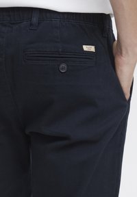 Dark navy pants made of cotton blend fabric, featuring a back pocket with a button, and a small label with "BLEND" stitched on it.