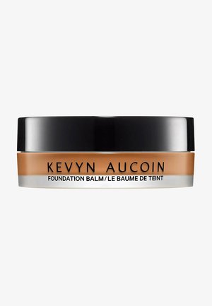 Kevyn Aucoin Foundation Balm in einem runden Glas mit einem schwarzen Deckel. Der Behälter hat einen beige-farbenen Boden mit silberner Schrift. Glatte, cremige Textur.