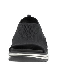 Schwarze Slippers mit gestricktem Obermaterial, offener Zehenpartie und strukturiertem Design. Sie verfügen über eine weiße gestreifte Sohle und eine kleine Zuglasche hinten.