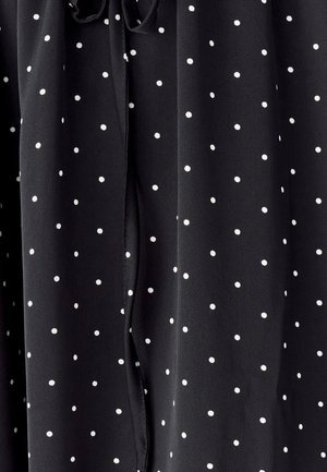 Black fabric with small white polka dots, featuring a smooth texture. The design includes delicate drapes and a tie detail at the neck.
