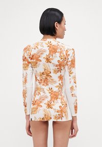 Long-sleeve floral swim shirt in white with orange and brown floral patterns, featuring a flat seam design and fitted silhouette.