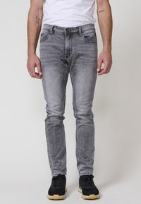 Šedé džíny z denimu s úzkým střihem, s vybledlým vzorem, designem s pěti kapsami a zapínáním na knoflík, v kombinaci s černými sportovními botami.
