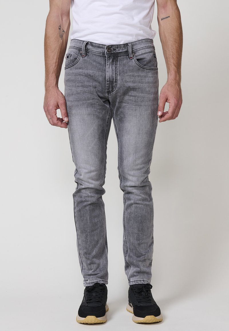 Šedé džíny z denimu s úzkým střihem, s vybledlým vzorem, designem s pěti kapsami a zapínáním na knoflík, v kombinaci s černými sportovními botami.