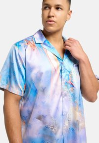 Short-sleeve shirt in lightweight, glossy fabric featuring a blue and pastel abstract pattern with circular and floral motifs, and a collar.