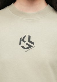 Hanorac bej deschis cu guler rotund. Dispune de un logo imprimat negru și de textul "KARL LAGERFELD JEANS" pe față. Textură a materialului moale.