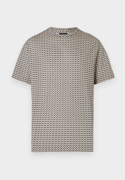 Μπεζ κοντομάνικο t-shirt με μαύρο ζιγκ-ζαγκ σχέδιο σε σχήμα κεραυνών, λαιμόκοψη τύπου crew, εμφανιζόμενο σε λευκό φόντο.