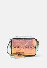 Rektangulär axelremsväska gjord av iriserande material. Har en tydlig logotyp "CALVIN KLEIN JEANS" på framsidan. Avtagbar rem.